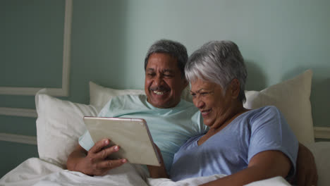 Glückliches-älteres-Mischlingspaar-Sitzt-Im-Bett-Mit-Tablet