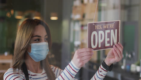Female-hairdresser-wearing-face-mask-changing-sign-board-Closed-to-Open-at-hair-salon