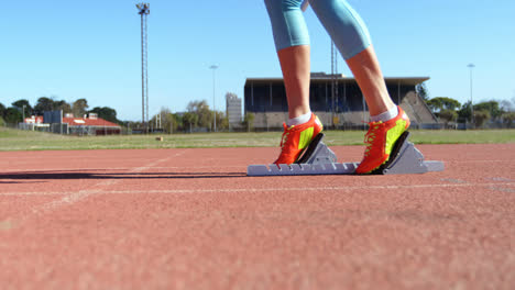 Low-section-of-female-athlete-taking-starting-position-on-a-running-track-on-a-running-track-at-spor