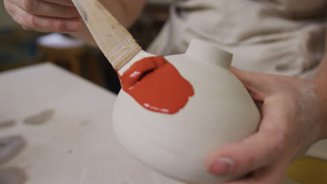 Close-up-view-of-female-potter-wearing-apron-using-glaze-brush-to-paint-on-pot-at-pottery-studio