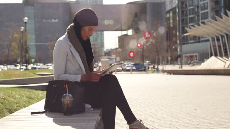 Animation-of-mixed-race-woman-wearing-hijab-in-street-using-tablet-computer-with-floating-heart-symb