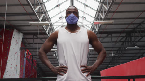 Fit-african-american-man-wearing-face-mask-standing-with-hands-on-his-hips-in-the-gym