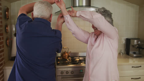 Senior-caucasian-couple-dancing-in-kitchen-in-slow-motion