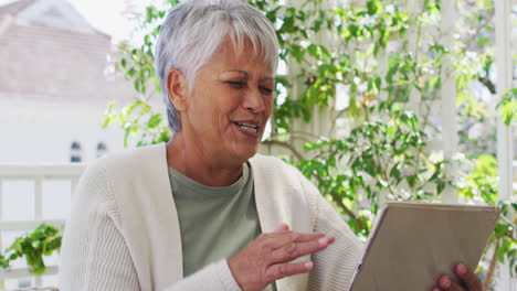 Ältere-Frau-Mit-Gemischter-Abstammung-Beim-Videochat-Mit-Tablet-Im-Garten