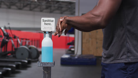 Mid-section-of-fit-african-american-man-sanitizing-his-hands-in-the-gym