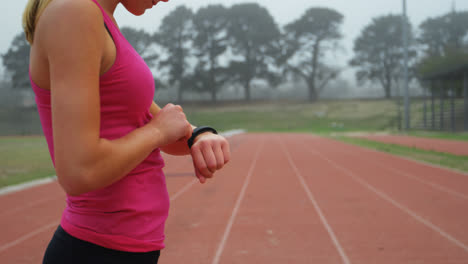 Side-view-of-Caucasian-female-athlete-using-smartwatch-on-running-track-at-sports-venue-4k