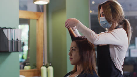 Female-hairdresser-wearing-face-mask-putting-rollers-on-hair-of-female-customer-at-hair-salon