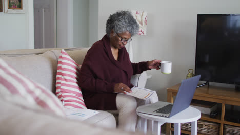 Ältere-Afroamerikanische-Frau-Trinkt-Kaffee,-Während-Sie-Zu-Hause-Ihre-Finanzen-Berechnet