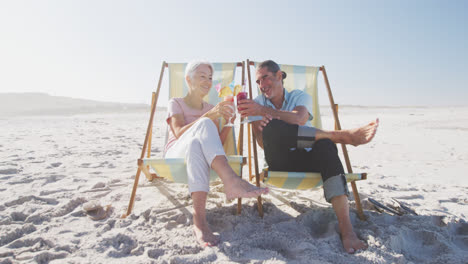 Senior-Caucasian-couple-sitting-on-sunbeds-at-the-beach.