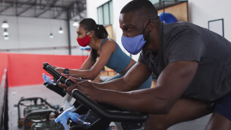 Diverse-woman-and-man-wearing-face-masks-exercising-at-gym