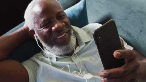 Afroamerikanischer-Mann,-Der-Sein-Smartphone-Benutzt,-Während-Er-Zu-Hause-Auf-Der-Couch-Liegt