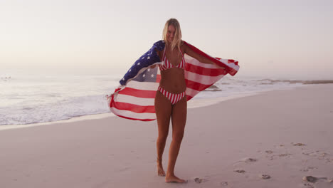 Mujer-Caucásica-Sosteniendo-Y-Ondeando-Una-Bandera-Estadounidense-En-La-Playa.