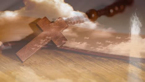 Animation-of-Christian-cross-over-rosary-beads,-clouds-with-wooden-surface-in-the-background