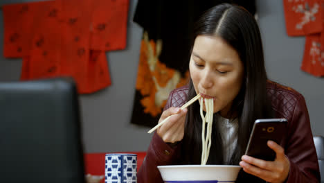 Woman-having-noodles-while-using-mobile-phone-4k