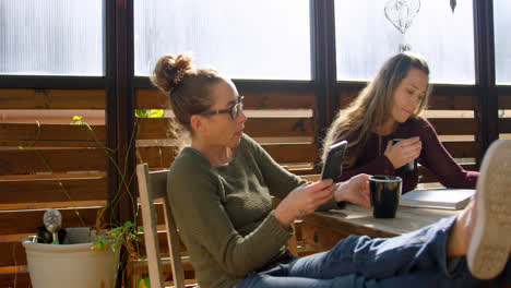 Lesbian-couple-using-mobile-phone-and-reading-book-while-having-coffee-4k