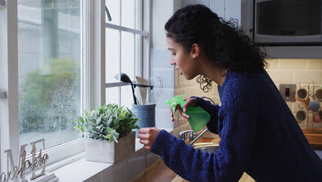 Mixed-race-woman-watering-plants-in-kitchen