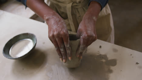 Close-up-view-of-female-potter-wearing-apron-working-on-clay-to-create-pot-at-pottery-studio