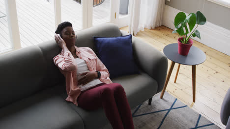 Afroamerikanische-Frau-Hört-Musik-über-Kopfhörer,-Während-Sie-Zu-Hause-Auf-Der-Couch-Liegt