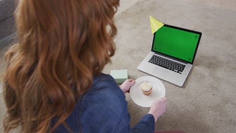 Frau-Mit-Partyhut-Bläst-Kerze-Auf-Den-Kuchen,-Während-Sie-Zu-Hause-Einen-Videochat-Auf-Dem-Laptop-Führt