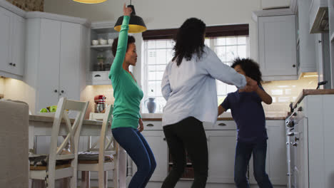 Mixed-race-lesbian-couple-and-daughter-dancing-in-kitchen