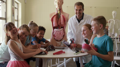 Profesor-Masculino-Y-Grupo-De-Niños-Sonriendo-En-Clase-De-Anatomía-Humana