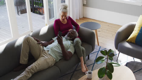 Älteres-Paar-Mit-Gemischter-Abstammung-Nutzt-Smartphone-Im-Wohnzimmer-Zu-Hause