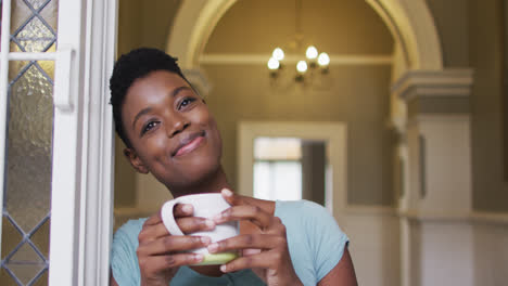 African-american-woman-holding-coffee-cup-smiling-at-home