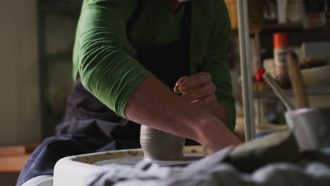 Mid-section-of-male-potter-creating-pottery-on-potters-wheel-at-pottery-studio