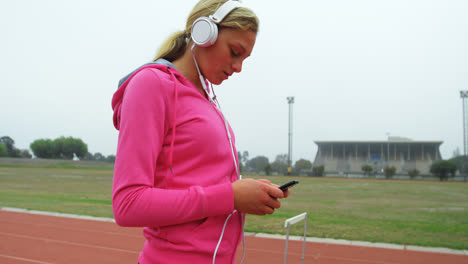 Side-view-of-Caucasian-female-athlete-listening-music-on-mobile-phone-at-sports-venue-4k