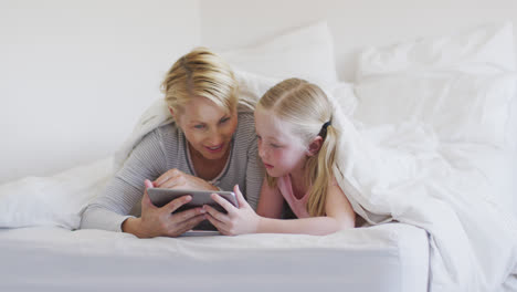 Front-view-of-Caucasian-woman-and-her-daughter-using-digital-tablet-on-bed-