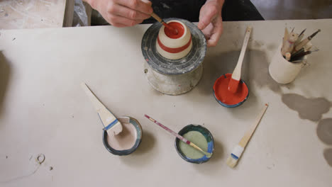 Overhead-view-of-male-potter-using-brush-to-paint-pot-on-potters-wheel-at-pottery-studio