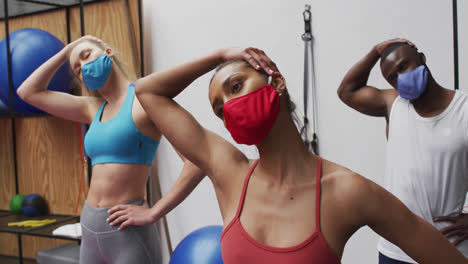 Diverse-fit-people-wearing-face-masks-performing-stretching-exercise-in-the-gym