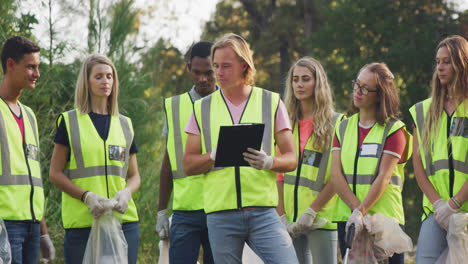 Mid-adults-with-yellow-vest-volunteering-and-man-taking-notes-during-river-clean-up-day