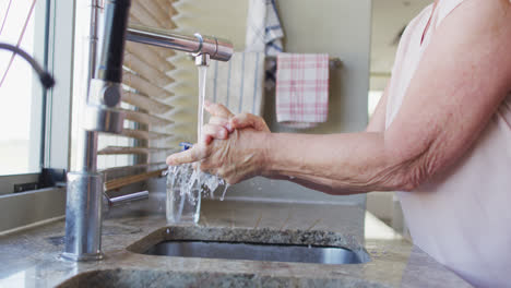 Mid-section-of-senior-caucasian-woman-washing-her-hands-in-the-sink-at-home