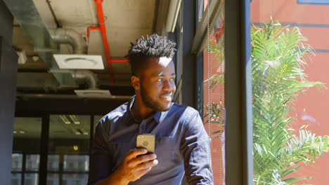Front-view-of-happy-young-black-businessman-looking-through-window-while-using-mobile-phone-4k