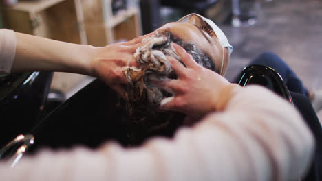 Female-hairdresser-washing-hair-of-female-customer-wearing-face-mask-at-hair-salon