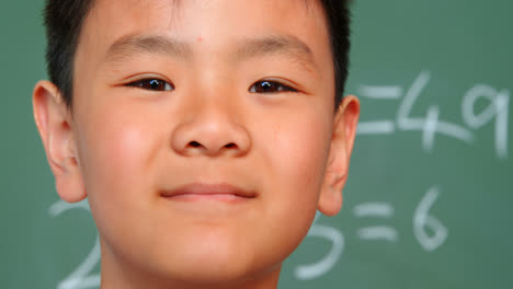 Close-up-of-Asian-schoolboy-standing-against-chalkboard-in-a-classroom-at-school-4k