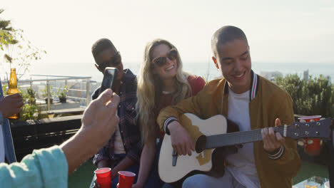 Young-man-playing-guitar-on-a-rooftop-with-his-friends