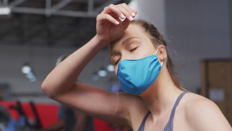 Caucasian-woman-wearing-face-mask-exercising-at-gym