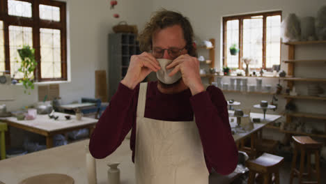 Portrait-of-male-caucasian-potter-wearing-face-mask-at-pottery-studio