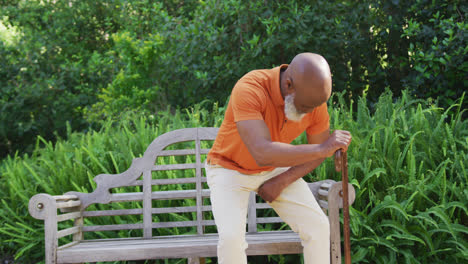 Afroamerikanischer-älterer-Mann-Mit-Gehstock-Sitzt-Auf-Einer-Bank-Im-Garten