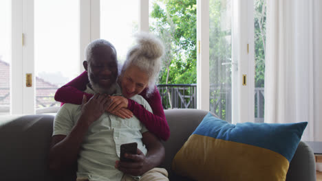 Älteres-Paar-Mit-Gemischter-Abstammung-Nutzt-Smartphone-Im-Wohnzimmer-Zu-Hause