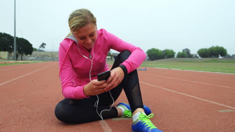 Front-view-of-Caucasian-female-athlete-listening-music-on-mobile-phone-at-sports-venue-4k