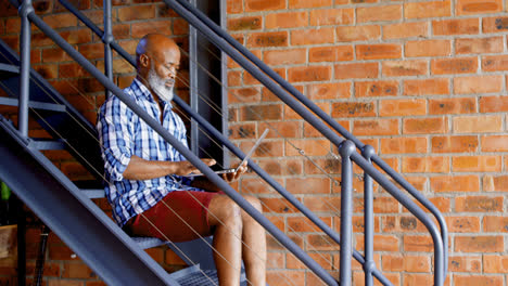 Senior-man-using-laptop-on-stairs-in-living-room-4k