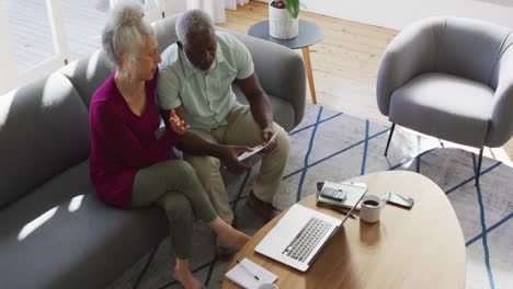 Mixed-race-senior-couple-discussing-finances-together-in-the-living-room-at-home