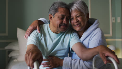 Smiling-senior-mixed-race-couple-embracing,-man-holding-walking-frame