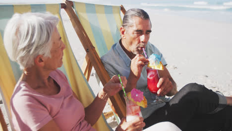 Senior-Caucasian-couple-sitting-on-sunbeds-at-the-beach.