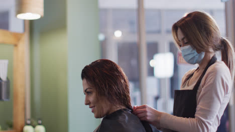 Female-hairdresser-wearing-face-mask-putting-cape-on-female-customer-at-hair-salon