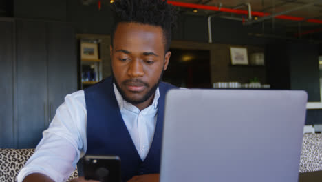 Front-view-of-young-black-businessman-working-on-mobile-phone-in-a-modern-office-4k
