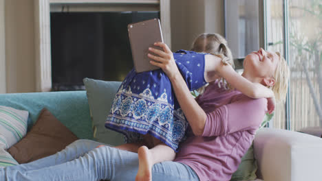 Side-view-of-Caucasian-woman-using-digital-tablet-and-playing-with-her-daughter-at-home